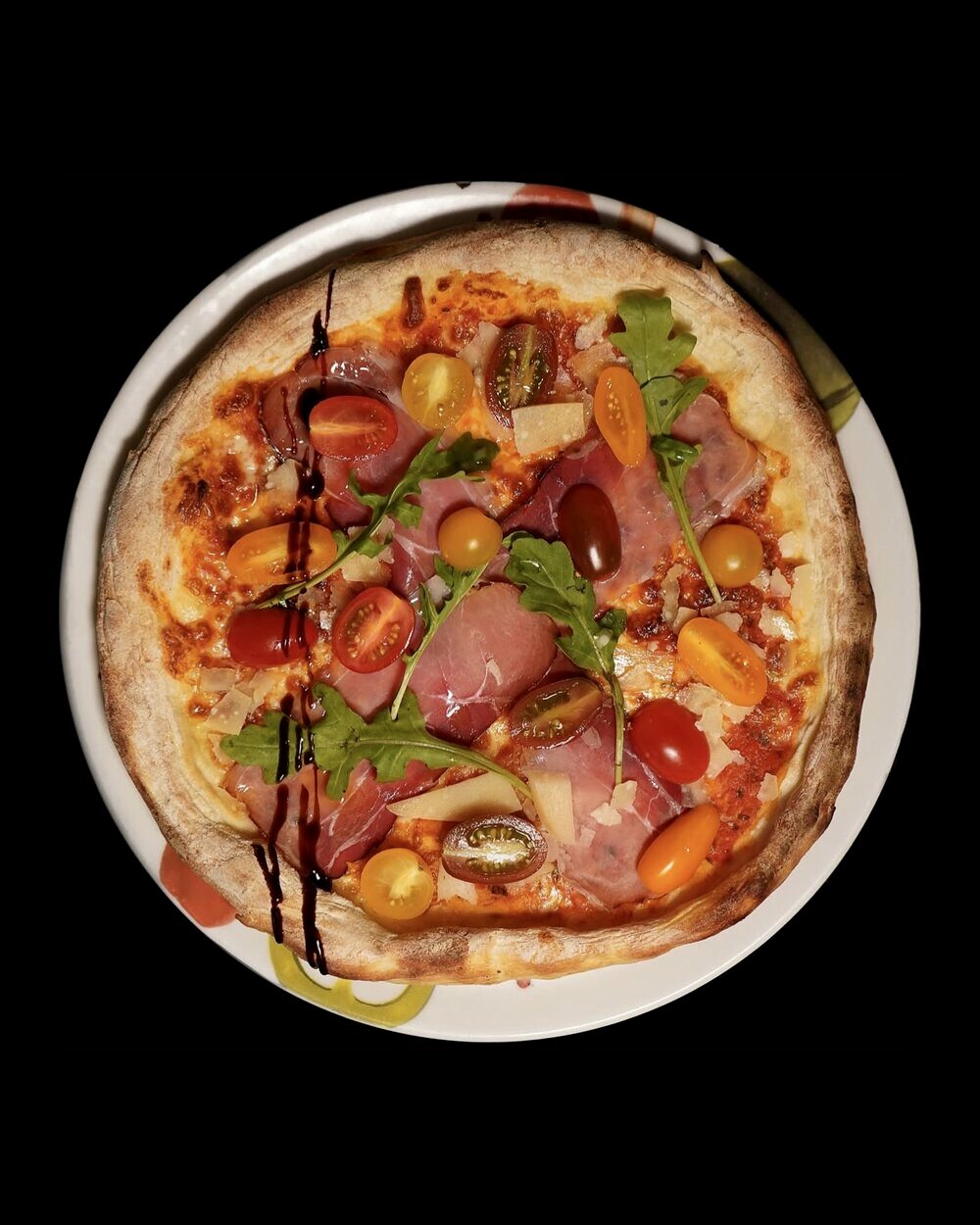 Pizza au jambon cru, copeaux de parmesan et roquette, cuite au four au Restaurant L’Étoile